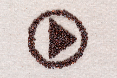 Bunch of roasted coffee beans forming play symbol enclosed in circle on creamy linen canvas, shot close upの写真素材