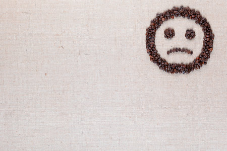 Sad round smile icon made of coffee beans on creamy linen texture, arranged top rightの写真素材