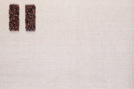 Bunch of roasted coffee beans forming pause symbol on creamy linen canvas, arranged top leftの写真素材