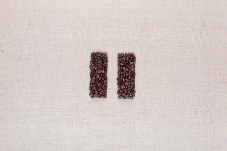 Bunch of roasted coffee beans forming pause symbol on creamy linen canvas, arranged in centerの写真素材