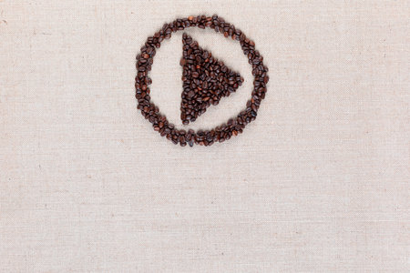 Bunch of roasted coffee beans forming play symbol enclosed in circle on creamy linen canvas, arranged top centerの写真素材
