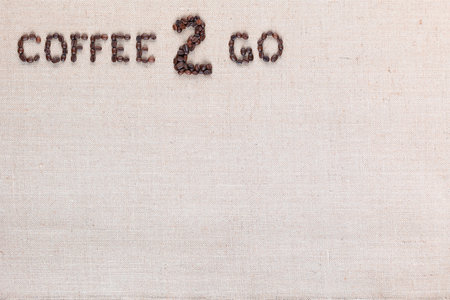 A lot of roasted seeds forming coffee to go writing against gray linen background, aligned top leftの写真素材