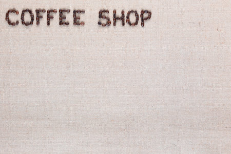 Bunch of roasted beans forming coffee shop inscription on gray canvas, aligned top leftの写真素材