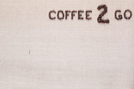 A lot of roasted seeds forming coffee to go writing against gray linen background, aligned top rightの写真素材