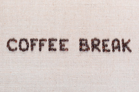 Roasted beans forming coffee break inscription on gray linen surface, shot close upの写真素材