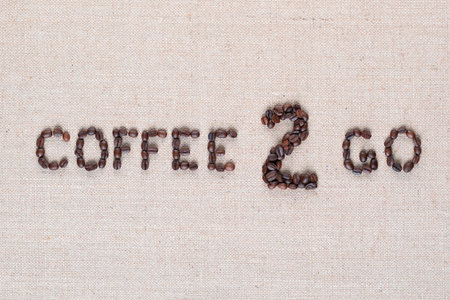 A lot of roasted seeds forming coffee to go writing against gray linen background, shot close upの写真素材