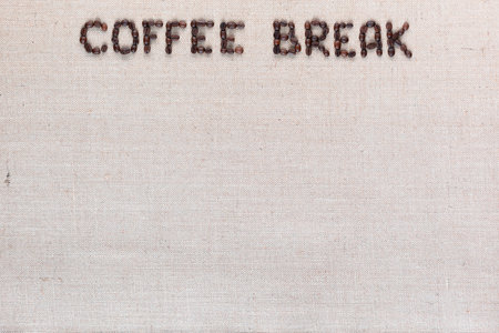 Roasted beans forming coffee break inscription on gray linen surface, aligned top centerの写真素材