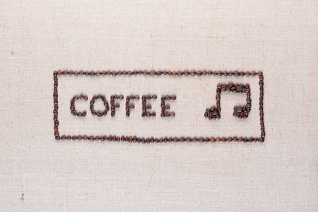Coffee word and music note made of roasted beans inside border on linen surface, aligned in centerの写真素材