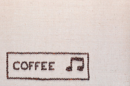 Coffee word and music note made of roasted beans inside border on linen surface, aligned bottom leftの写真素材