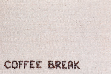 Roasted beans forming coffee break inscription on gray linen surface, aligned bottom leftの写真素材