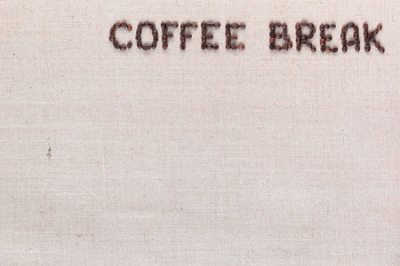 Roasted beans forming coffee break inscription on gray linen surface, aligned top rightの写真素材