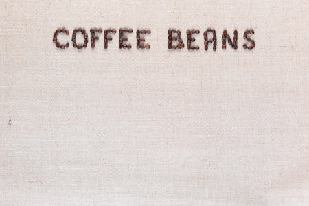 Many roasted seeds forming coffee beans writing against gray canvas background, aligned top centerの写真素材