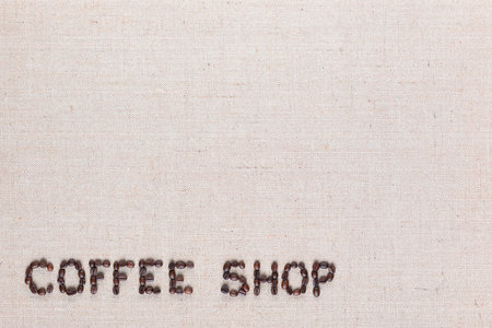 Bunch of roasted beans forming coffee shop inscription on gray canvas, aligned bottom leftの写真素材