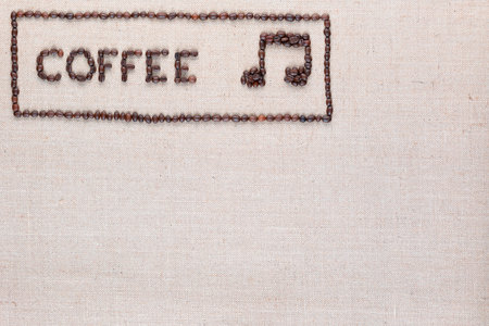 Coffee word and music note made of roasted beans inside border on linen surface, aligned top leftの写真素材
