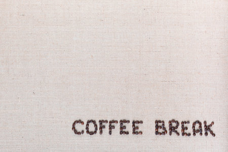 Roasted beans forming coffee break inscription on gray linen surface, aligned bottom rightの写真素材
