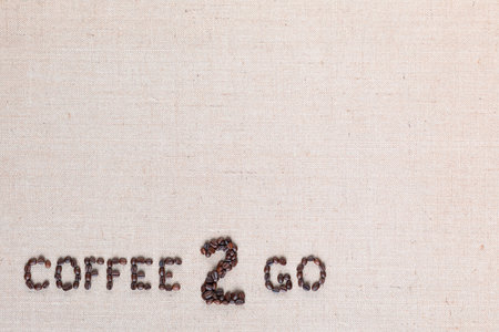 A lot of roasted seeds forming coffee to go writing against gray linen background, aligned bottom leftの写真素材