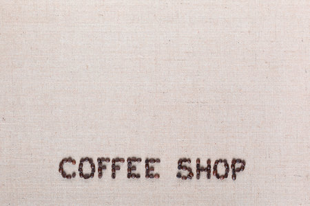 Bunch of roasted beans forming coffee shop inscription on gray canvas, aligned bottom centerの写真素材