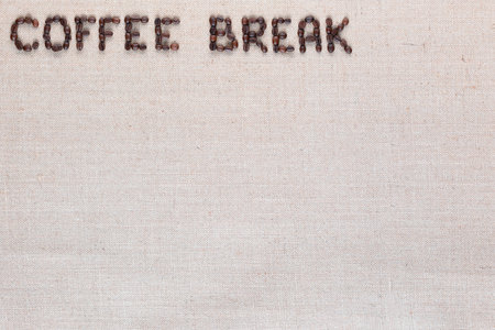 Roasted beans forming coffee break inscription on gray linen surface, aligned top leftの写真素材