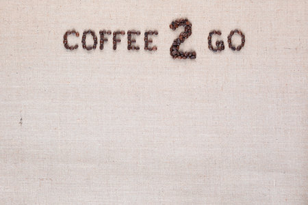A lot of roasted seeds forming coffee to go writing against gray linen background, aligned top centerの写真素材