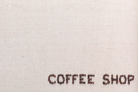 Bunch of roasted beans forming coffee shop inscription on gray canvas, aligned bottom rightの写真素材