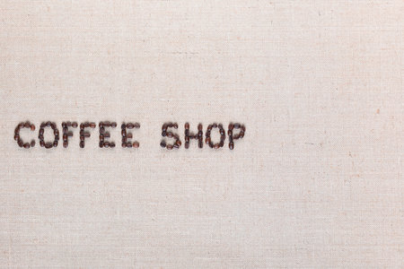 Bunch of roasted beans forming coffee shop inscription on gray canvas, aligned middle leftの写真素材