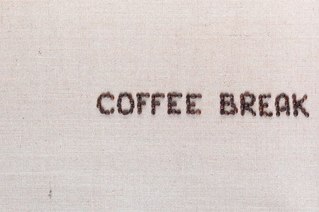 Roasted beans forming coffee break inscription on gray linen surface, aligned middle rightの写真素材