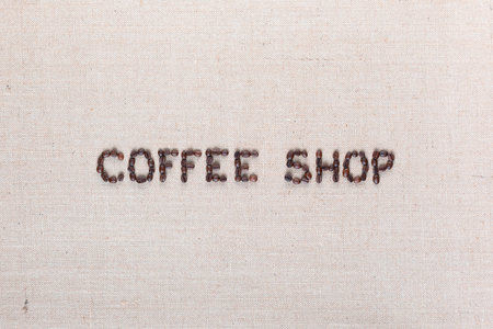 Bunch of roasted beans forming coffee shop inscription on gray canvas, aligned in centerの写真素材