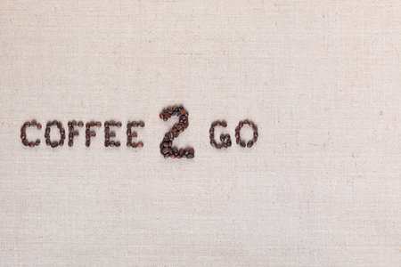 A lot of roasted seeds forming coffee to go writing against gray linen background, aligned middle leftの写真素材