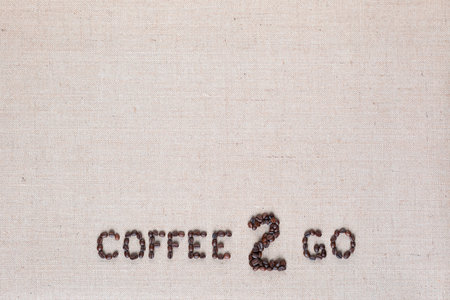 A lot of roasted seeds forming coffee to go writing against gray linen background, aligned bottom centerの写真素材