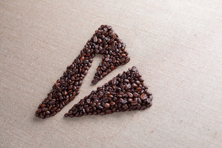 Letter y enclosed in triangle shape made of roasted coffee beans on creamy linen texture, aligned in perspective, with light source from aboveの写真素材