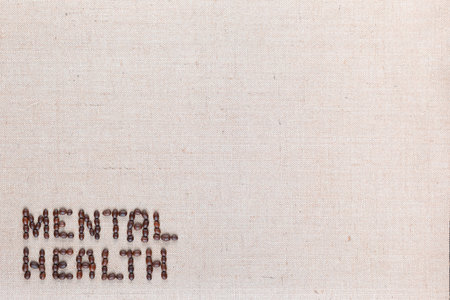 Mental health inscription made of roasted coffee beans placed on creamy linen texture, aligned bottom leftの写真素材