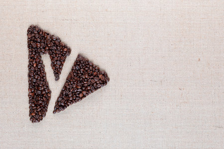 Letter y enclosed in triangle shape made of roasted coffee beans on creamy linen texture, aligned to the leftの写真素材