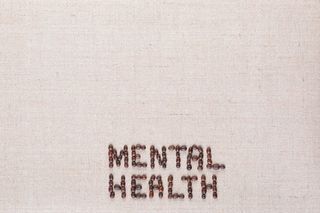 Mental health inscription made of roasted coffee beans placed on creamy linen texture, aligned bottom centerの写真素材