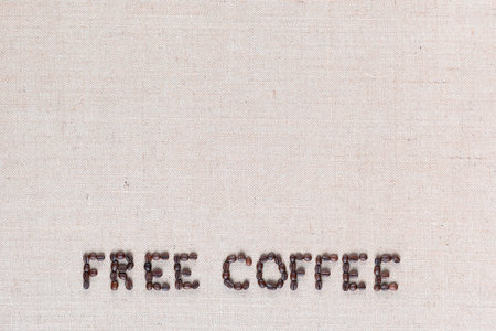 Free coffee written with roasted coffee beans on creamy linen texture, aligned bottom centerの写真素材