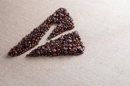 Letter y enclosed in triangle shape made of roasted coffee beans on creamy linen texture, aligned in perspectiveの写真素材