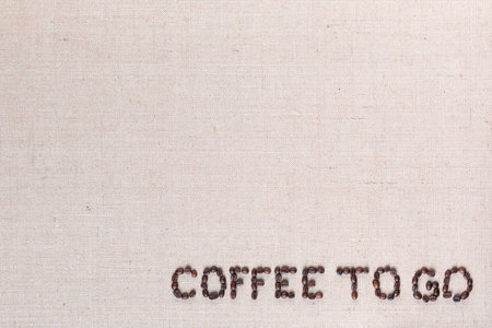 Coffee to go inscription made of roasted coffee beans on creamy linen canvas, aligned bottom rightの写真素材