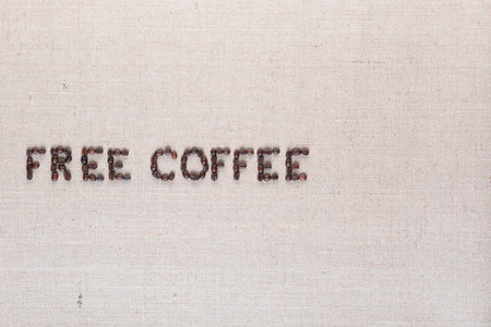 Free coffee written with roasted coffee beans on creamy linen texture, aligned middle leftの写真素材