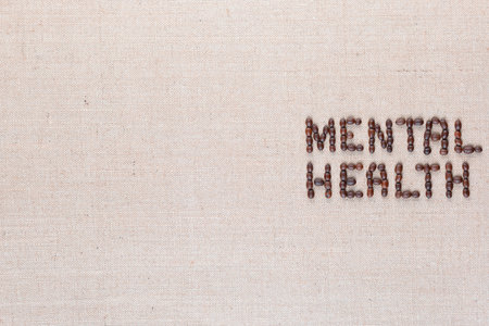 Mental health inscription made of roasted coffee beans placed on creamy linen texture, aligned middle rightの写真素材