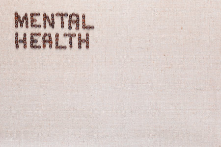 Mental health inscription made of roasted coffee beans placed on creamy linen texture, aligned top leftの写真素材