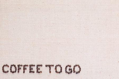 Coffee to go inscription made of roasted coffee beans on creamy linen canvas, aligned bottom leftの写真素材
