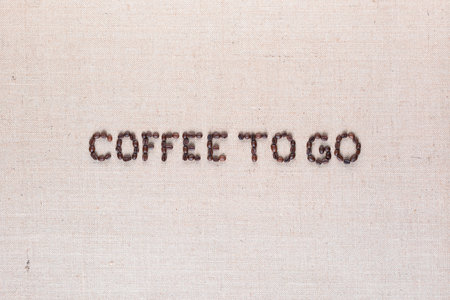 Coffee to go inscription made of roasted coffee beans on creamy linen canvas, aligned in centerの写真素材