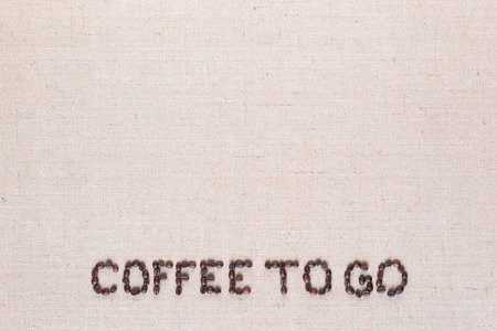 Coffee to go inscription made of roasted coffee beans on creamy linen canvas, aligned bottom centerの写真素材