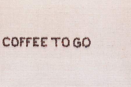 Coffee to go inscription made of roasted coffee beans on creamy linen canvas, aligned middle leftの写真素材