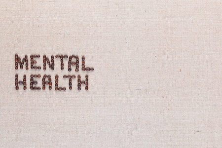 Mental health inscription made of roasted coffee beans placed on creamy linen texture, aligned middle leftの写真素材