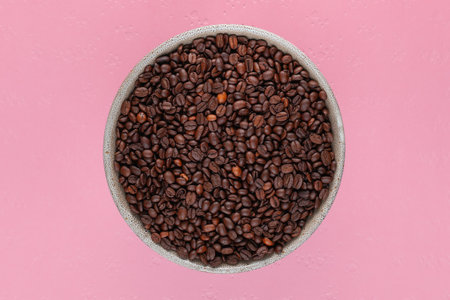 Close up of grey cup full with roasted coffee beans on pink textured backgroundの写真素材