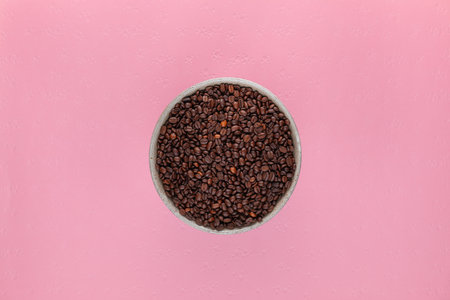 Grey cup full with roasted coffee beans on pink textured backgroundの写真素材
