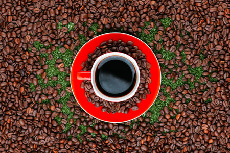 Close up of a coffee mug on red plate full of beans surrounded by many roasted coffee seedsの写真素材
