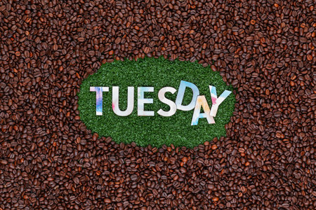 Tuesday written with colorful letters, arranged playful on artificial grass surrounded by roasted coffee beansの写真素材