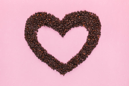 Bunch of coffee beans forming a hollow heart on a pink textured backgroundの写真素材