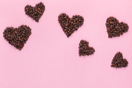 Multiple small hearts made of roasted coffee beans on pink textured backgroundの写真素材